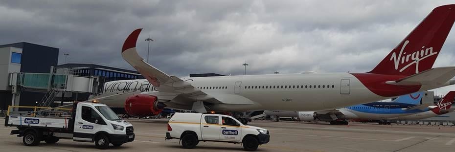 Bethell van parked on a runway in front of a passenger jet