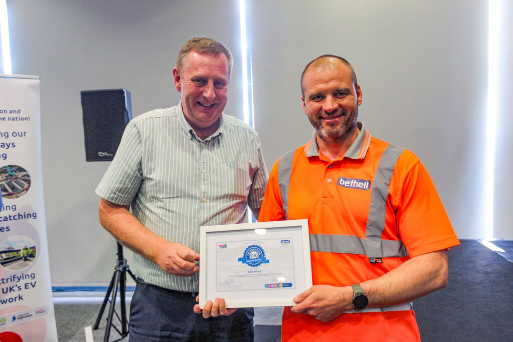 An operative in orange PPE is handed a service recognition award