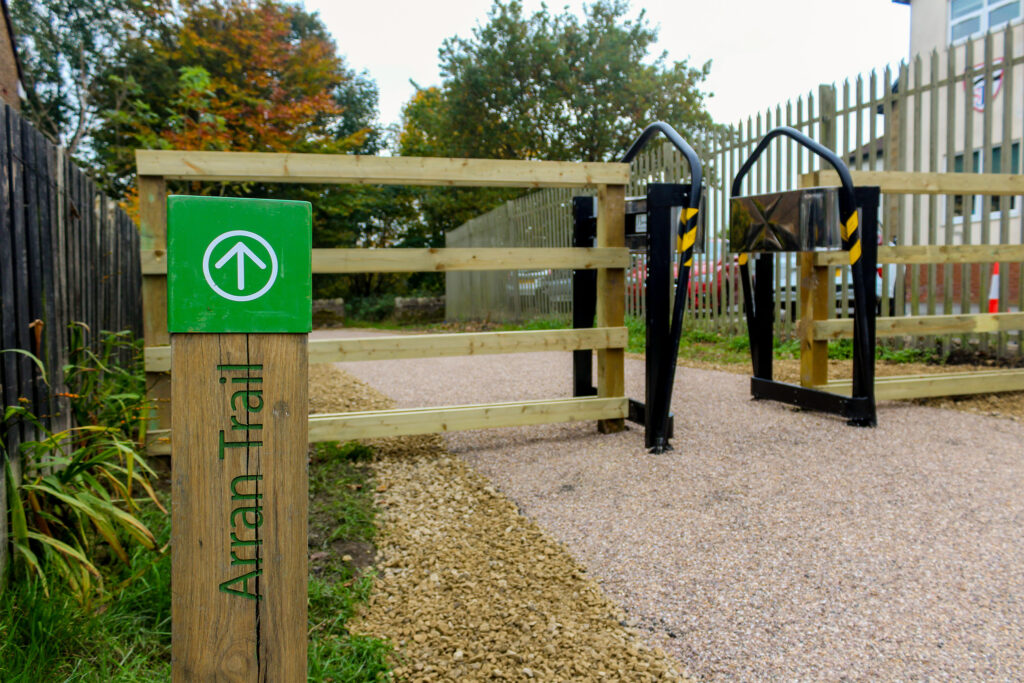 A wooden bollard directing pedestrians to a footpath with a gated entrance